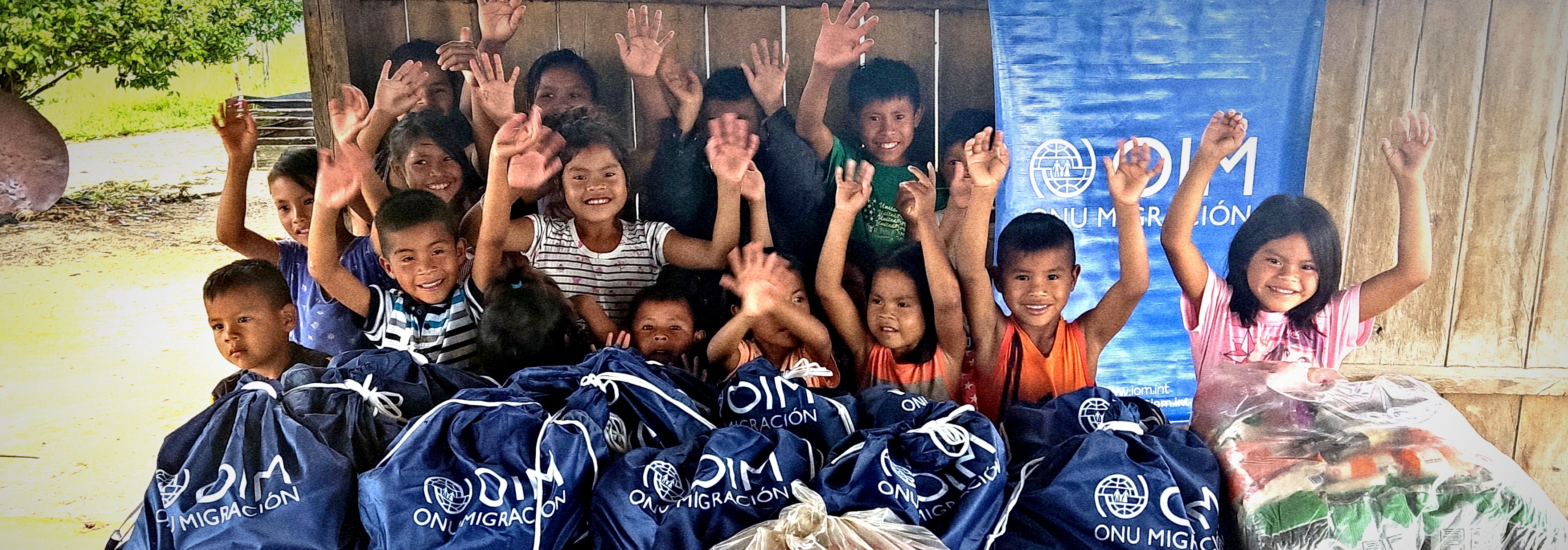 Group of children waving behind food items that IOM and its local implementing partner distributed in the indigenous community of Gran Sabana municipality, Bolivar State. © IOM 2022 / Haysariz Alexandra Gonzalez Lozano