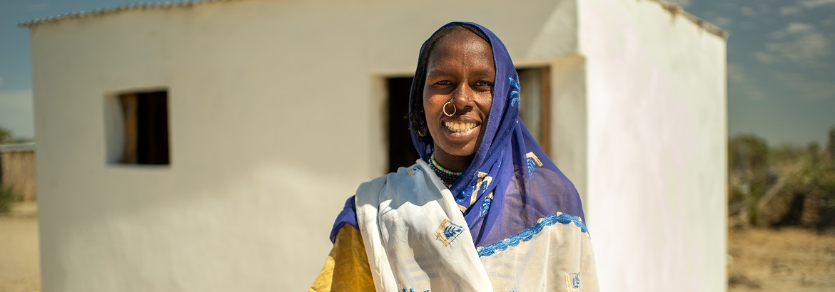 A woman who has received shelter support stands in front of her house in Lake Chad province, Chad. @ IOM Chad, 2021
